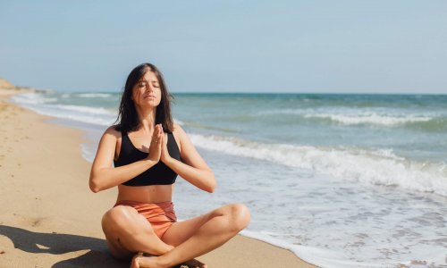 Mental health and self care concept. Young beautiful woman practicing yoga on the beach, sitting on sand and meditaning. Happy girl relaxing on seashore on summer vacation